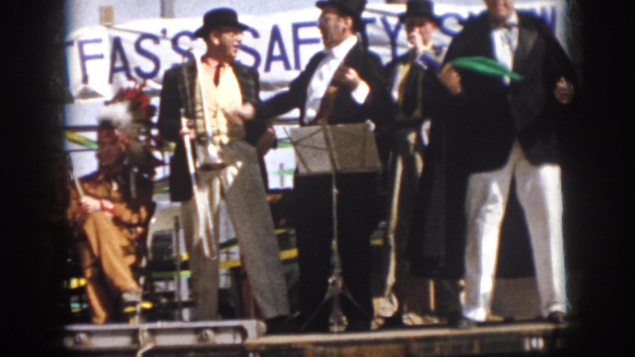 1958 Virginia home-movie frame of performers pausing on a parade float, with trombone, music stand, and seated players visible.
