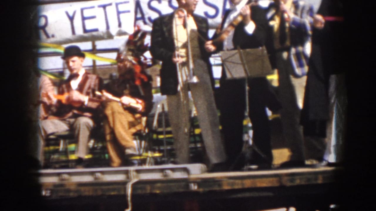 1958 Virginia 8mm frame showing seated string players and standing band members on a decorated parade float.