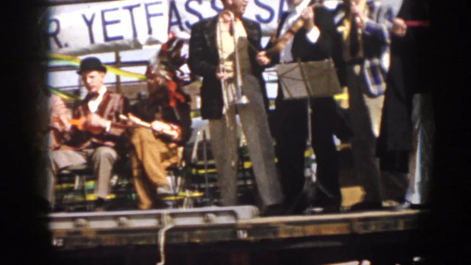 1958 Virginia 8mm frame showing seated string players and standing band members on a decorated parade float.