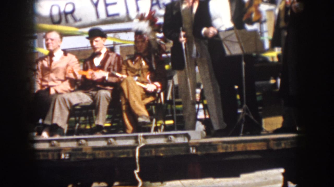 1958 Virginia home-movie frame showing men on a truck float, including musicians and a performer in a Native American-style headdress.