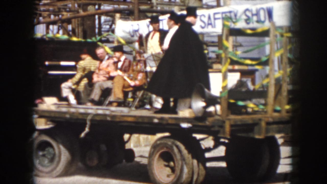 1958 Virginia frame of a moving parade float with costumed men, a hand-painted SAFETY SHOW banner, ribbons, and loudspeaker equipment.