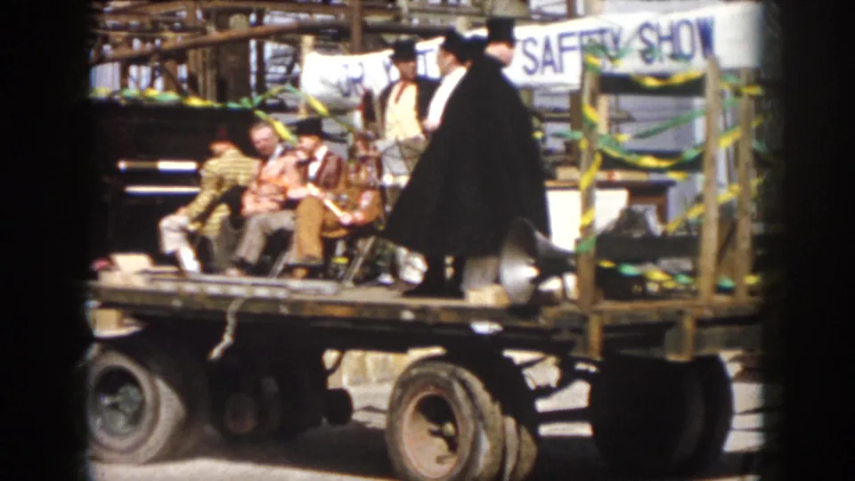 1958 Virginia frame of a moving parade float with costumed men, a hand-painted SAFETY SHOW banner, ribbons, and loudspeaker equipment.