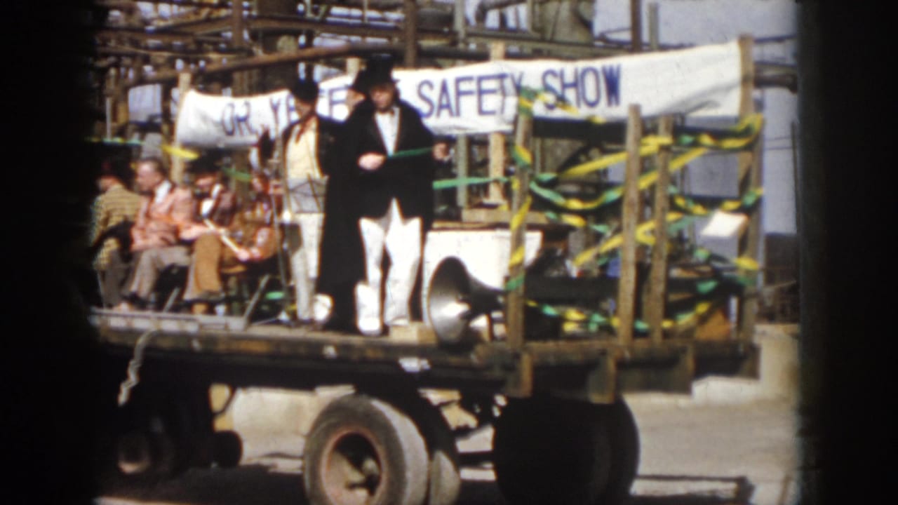 1958 Virginia home-movie frame showing two top-hatted men on a decorated safety-show float with seated participants behind them.