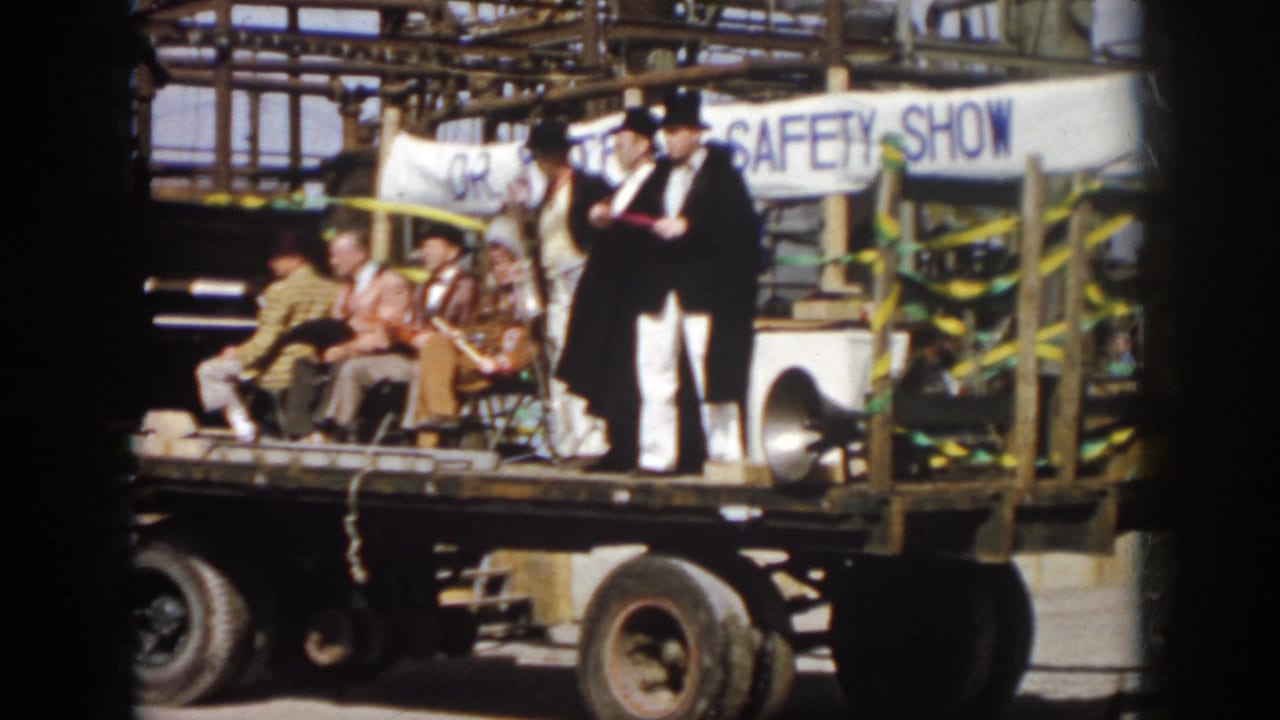 1958 Virginia frame of a safety-show parade float with seated men, caped top-hatted performers, ribbons, and a visible truck chassis.