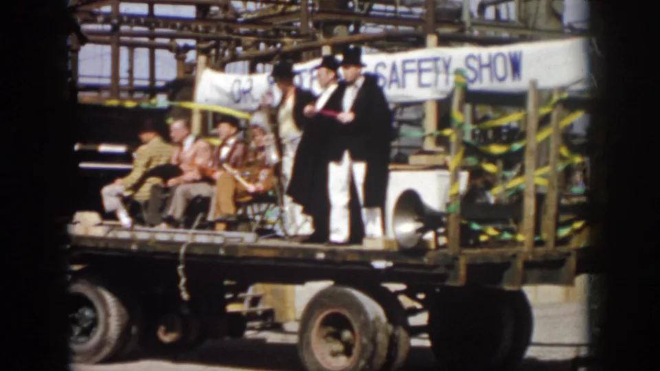 1958 Virginia frame of a safety-show parade float with seated men, caped top-hatted performers, ribbons, and a visible truck chassis.