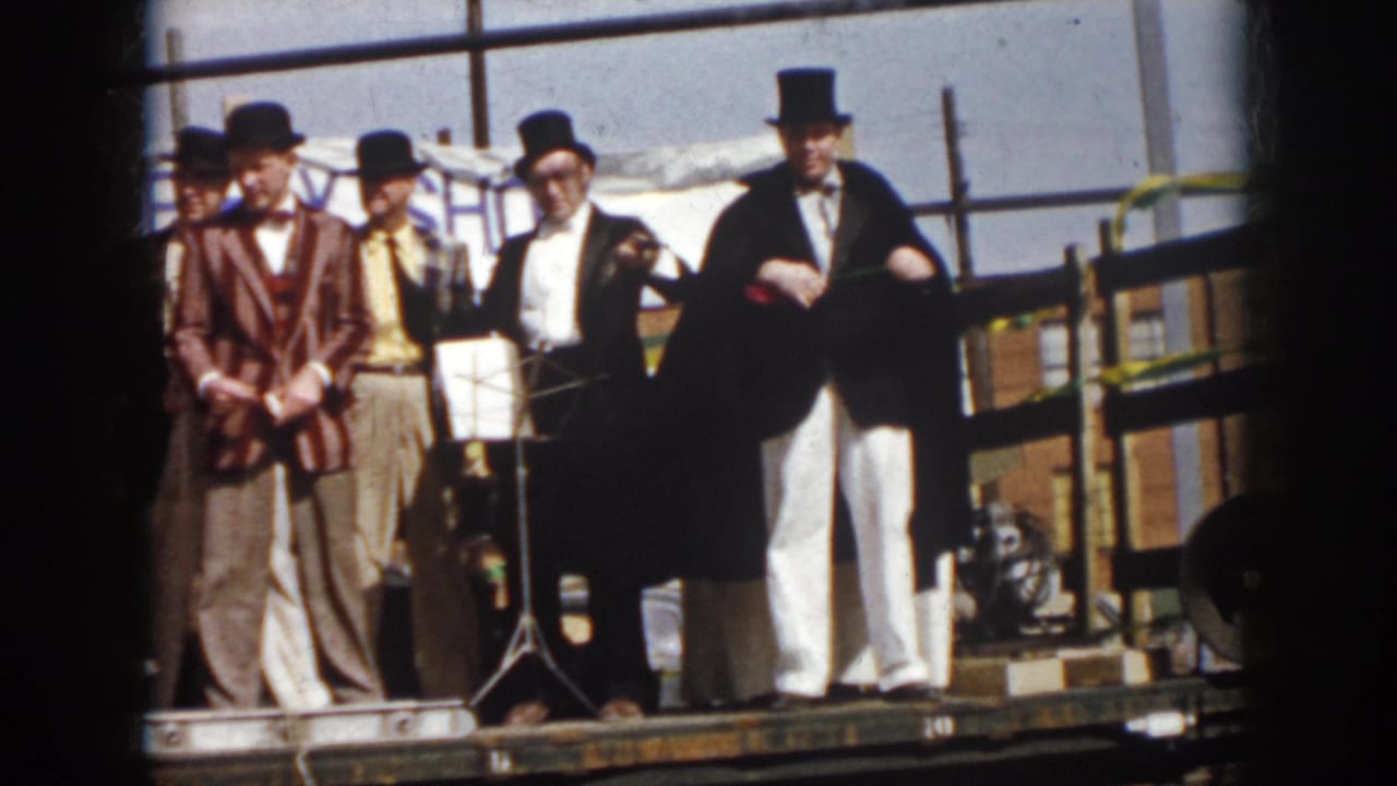 Costumed male entertainers in top hats stand on a Virginia parade truck, with instruments, a music stand, and a banner behind them.