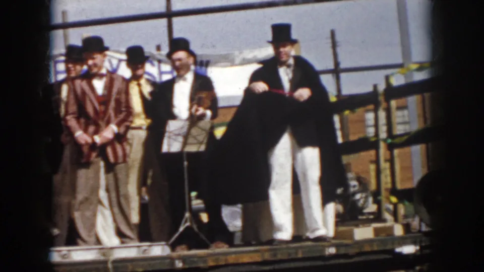 1958 Virginia parade scene with entertainers in top hats and formal clothing beside a caped performer on a flatbed truck.