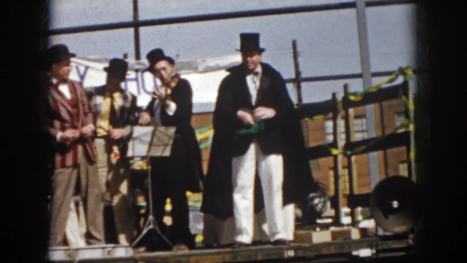 Virginia 1958 parade footage showing top-hatted entertainers on a truck, including a caped figure holding a green handkerchief.