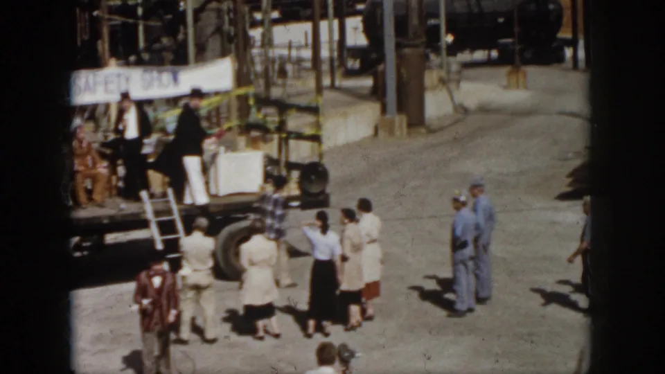 1958 Virginia frame showing workers gathered below a flatbed truck stage with performers and safety-show signage visible.