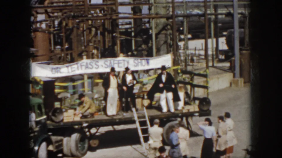 1958 Virginia frame showing the Dr. Tefas safety show on a flatbed truck, with spectators below and industrial equipment in the background.