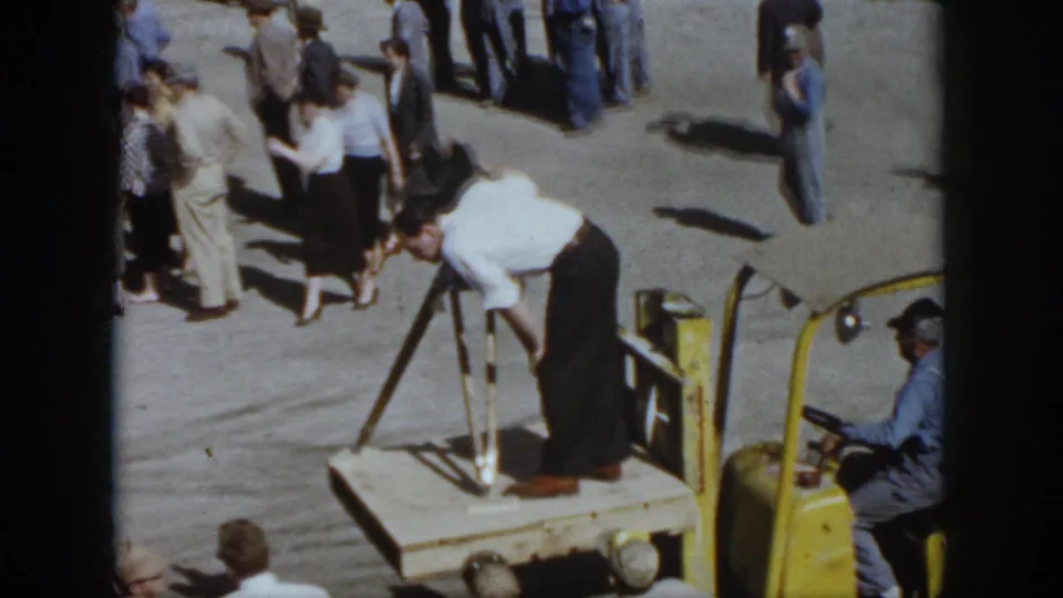 Virginia 1958 home-movie view of workers gathered around a wooden platform and yellow forklift during an outdoor industrial demonstration.