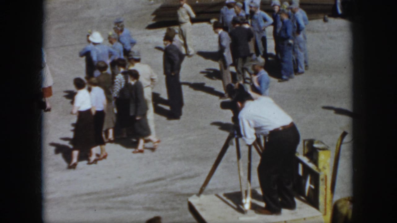 1958 Virginia home-movie frame showing adults gathered on pavement while a man in a white shirt films from a tripod camera.