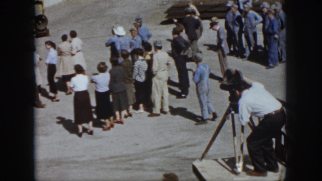 Adults gather on pavement near a tripod camera and camera operator.