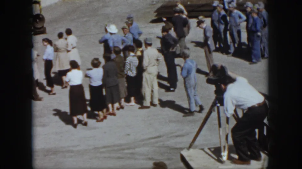 1958 Virginia outdoor event scene with adults in mid-century clothing standing near a tripod-mounted camera.