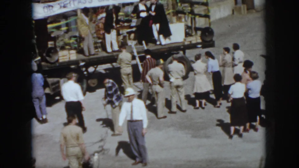 1958 Virginia home-movie frame showing people watching a flatbed truck stage beneath a safety-show banner.