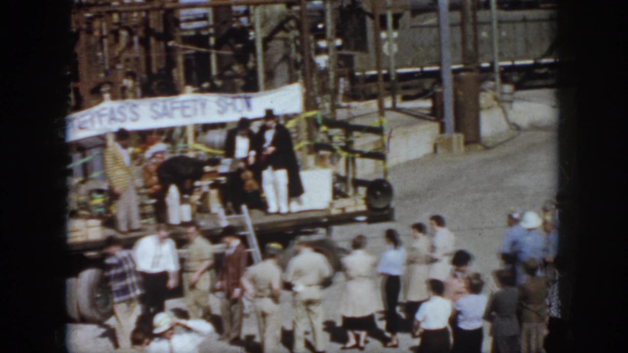 1958 Virginia rail-yard crowd watches a small outdoor safety-show stage with freight cars and industrial structures behind it.