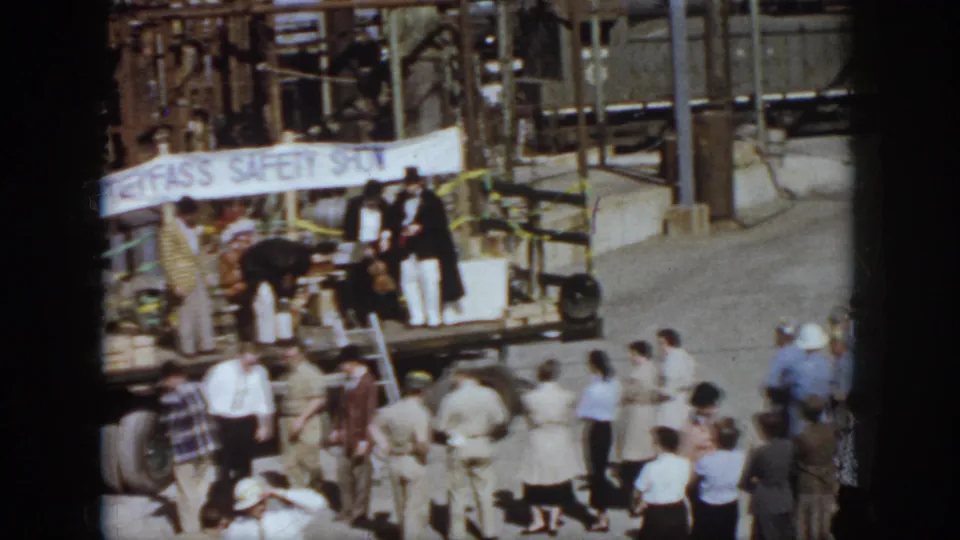 1958 Virginia rail-yard crowd watches a small outdoor safety-show stage with freight cars and industrial structures behind it.