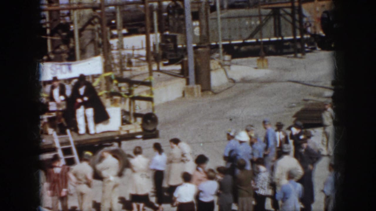 People face a small platform with a safety banner in an industrial rail yard.