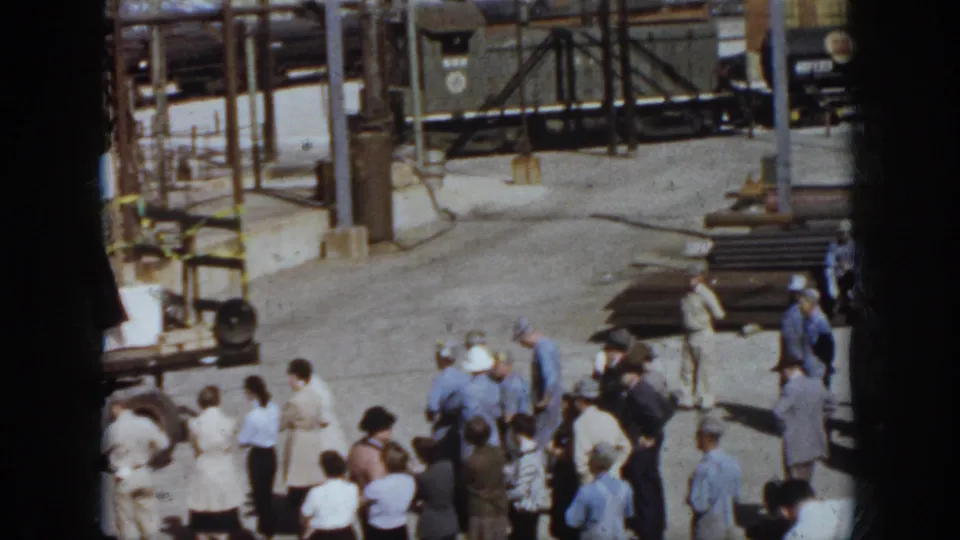 Rail-yard spectators in 1958 Virginia stand near the edge of a safety-show stage, with freight cars and stacked materials nearby.