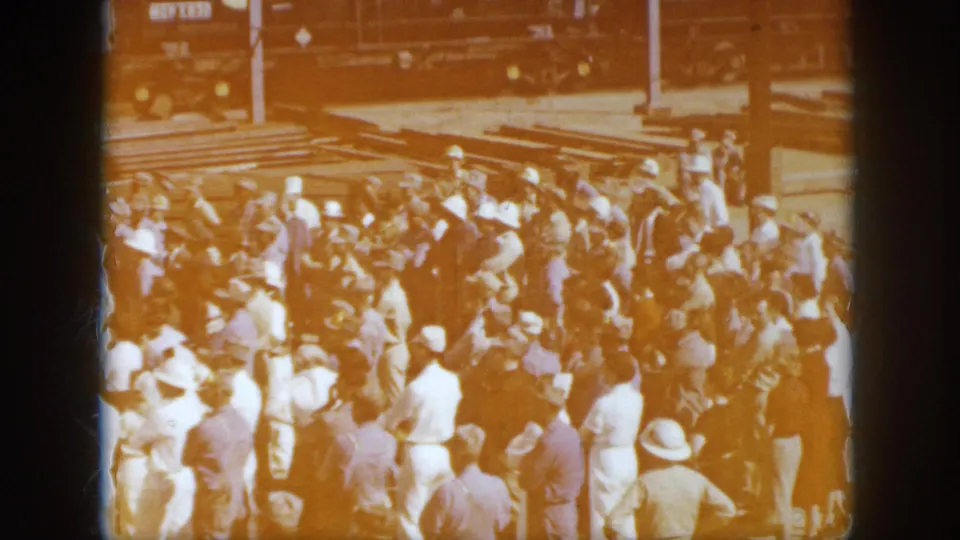 A larger group of adults in a 1958 Virginia railway yard gathers near tracks and freight cars, recorded with warm 8mm exposure.