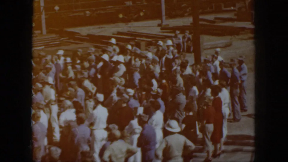 1958 Virginia home-movie frame showing adults gathered near railroad tracks and a freight train, partly obscured by warm lens flare.