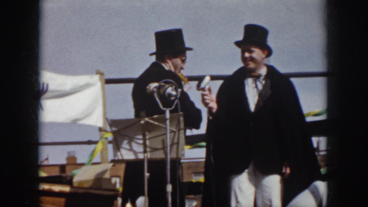 1958 Virginia home-movie frame with one performer holding a microphone toward another man in a top hat near a standing microphone.