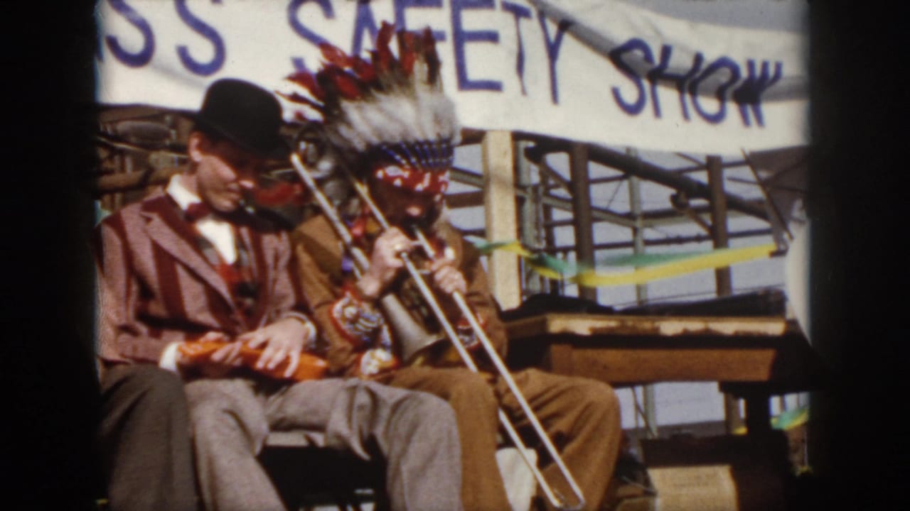 1958 Virginia home-movie frame with a bowler-hatted violinist seated beside a trombone player in a Native American-style headdress.