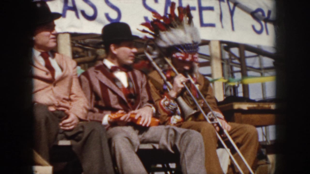 Three men on a stage, two in suits and bowler hats beside a trombone player wearing a headdress.