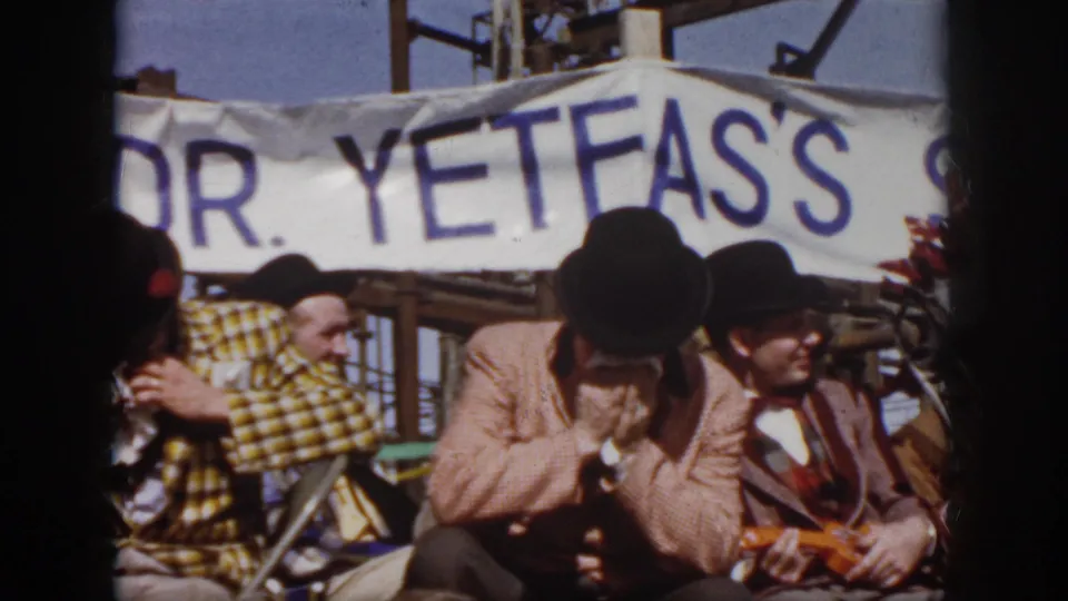 Costumed festival performers in top hats sit below a white banner that appears to read "DR. YETFA'S."