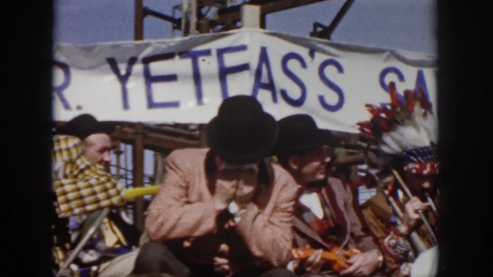 1958 Virginia festival frame with a harmonica player, a seated top-hatted musician, and feathered headwear beside the band.