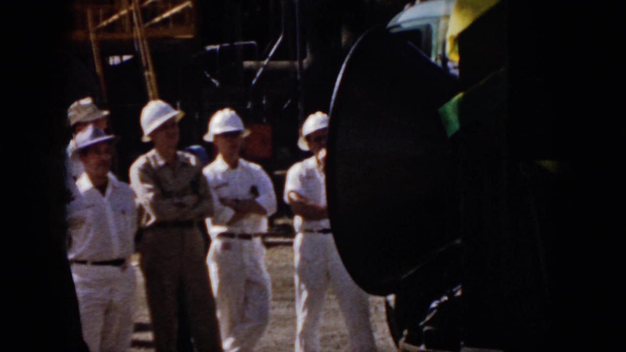 1958 Virginia factory or plant scene with men in hard hats and work uniforms listening near large black speakers.