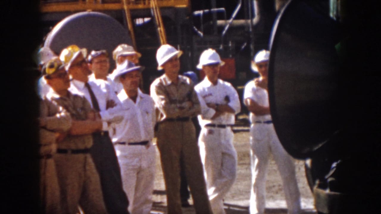 Group of men in white hard hats and khaki uniforms stand with arms crossed near speakers.