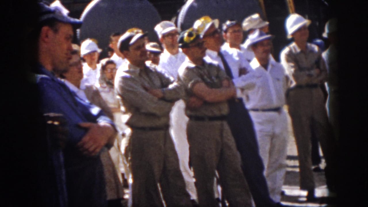 1958 Virginia home-movie frame showing uniformed men and visitors standing in bright sun near industrial tanks.