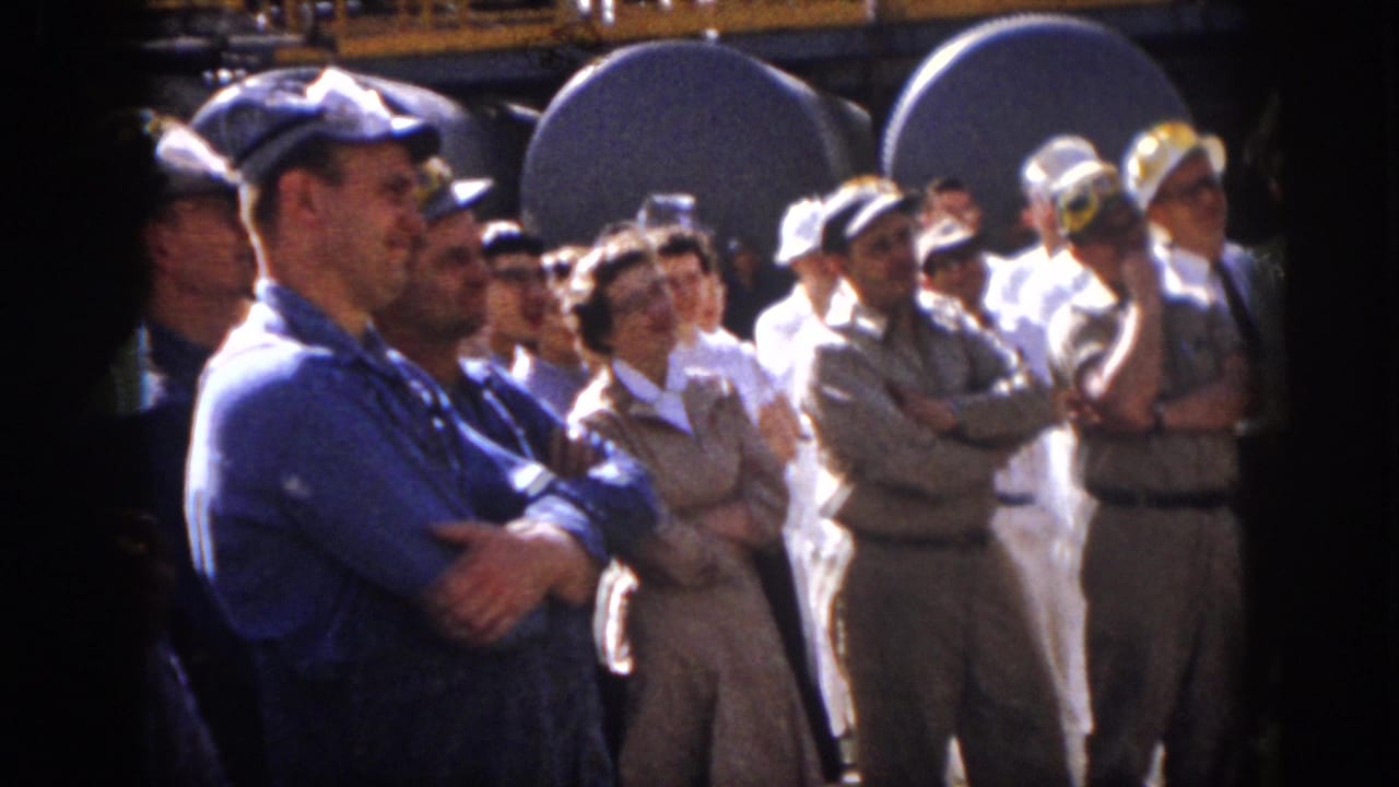 1958 Virginia home-movie frame showing workers and visitors clapping in a crowded industrial yard.