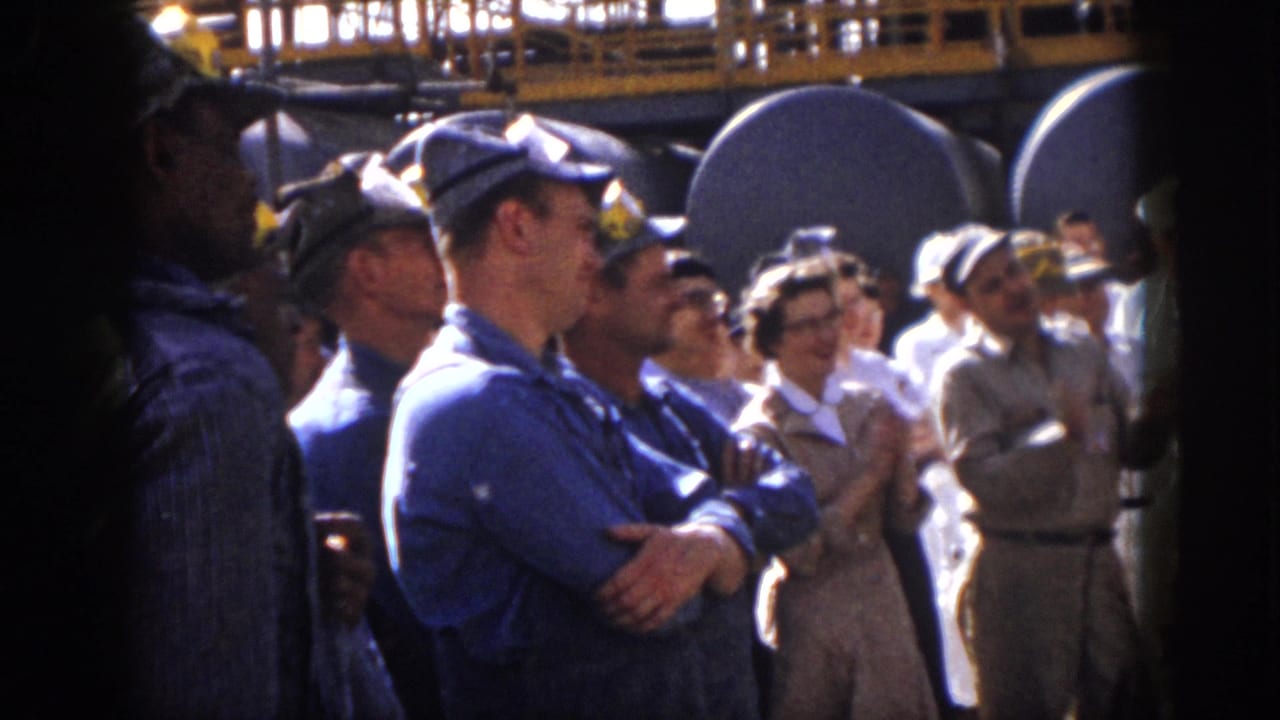 1958 Virginia frame with uniformed workers, visitors, and hard-hatted men applauding near large tanks.