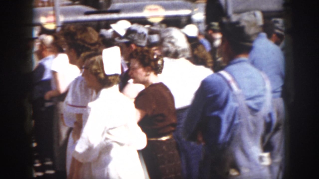 1958 Virginia frame showing nurses in white uniforms assisting or escorting a woman within a crowded outdoor industrial setting.