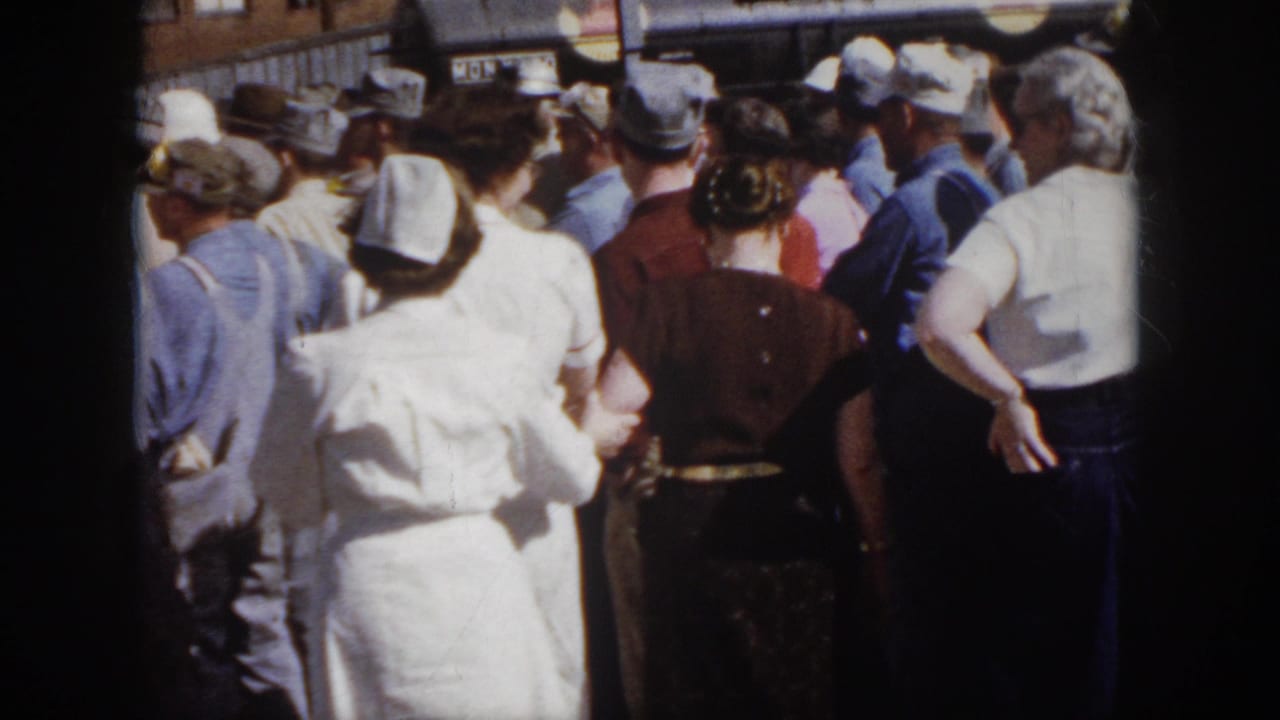 1958 Virginia home-movie view from behind a dense crowd, with nurses, workers, and bystanders facing activity near industrial equipment.