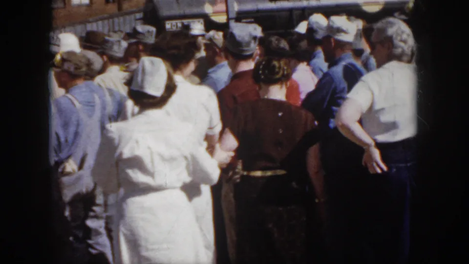 1958 Virginia home-movie view from behind a dense crowd, with nurses, workers, and bystanders facing activity near industrial equipment.