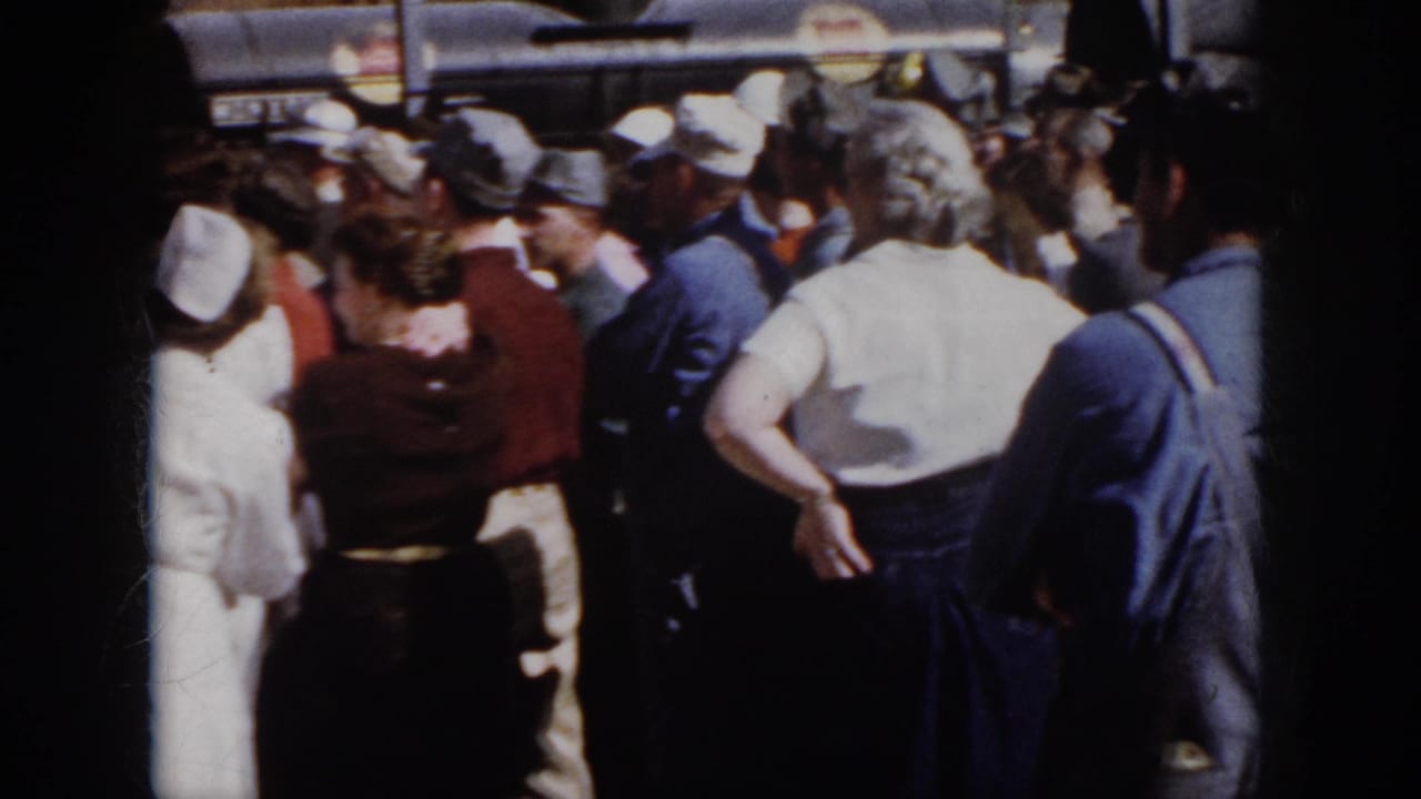 1958 Virginia frame showing a crowded outdoor workplace gathering as nurses and workers remain clustered around an unseen central moment.