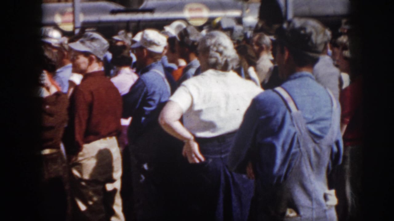 1958 Virginia home-movie frame showing adults in mid-century clothing standing close together at an outdoor community gathering.