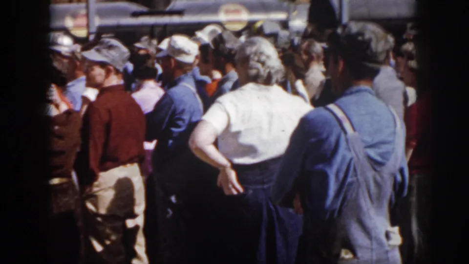 1958 Virginia home-movie frame showing adults in mid-century clothing standing close together at an outdoor community gathering.