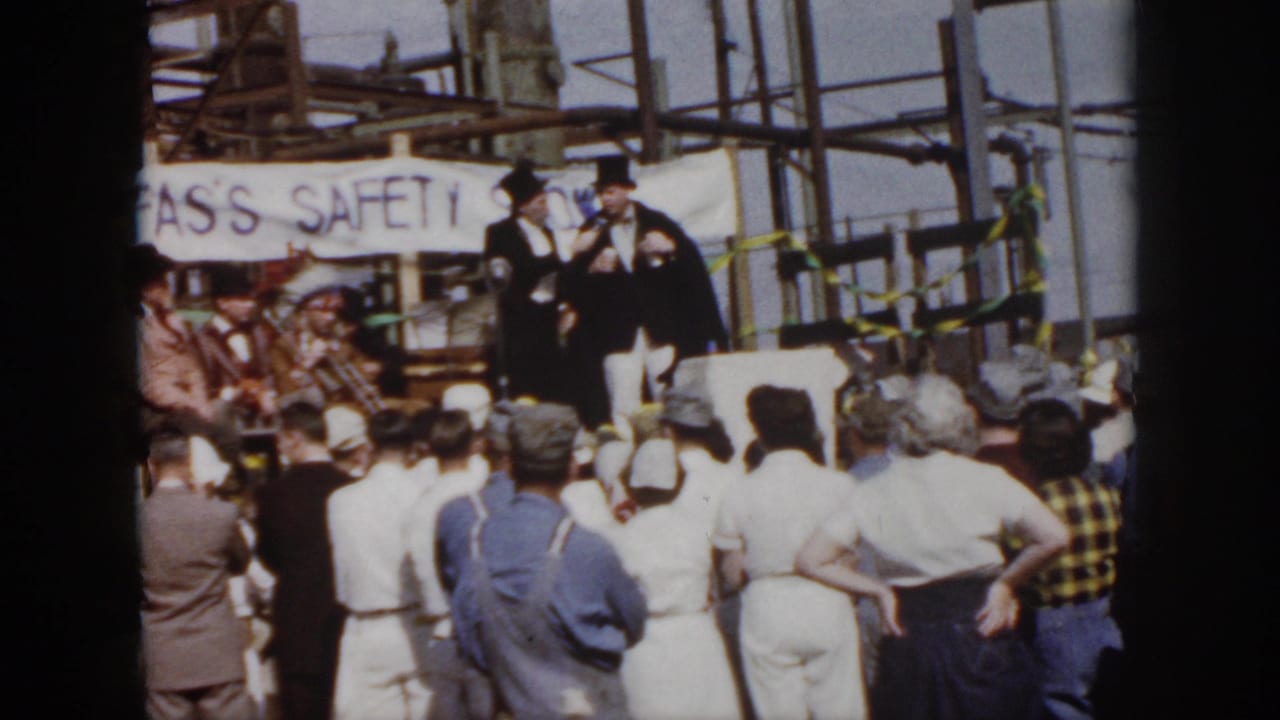 1958 Virginia home-movie frame showing an industrial safety ceremony with a standing crowd, top-hatted men, and a partly visible safety banner.