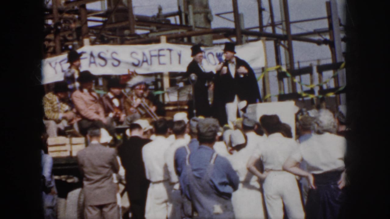 1958 Virginia frame showing workers and spectators gathered at an outdoor industrial safety ceremony with speakers on a small stage.