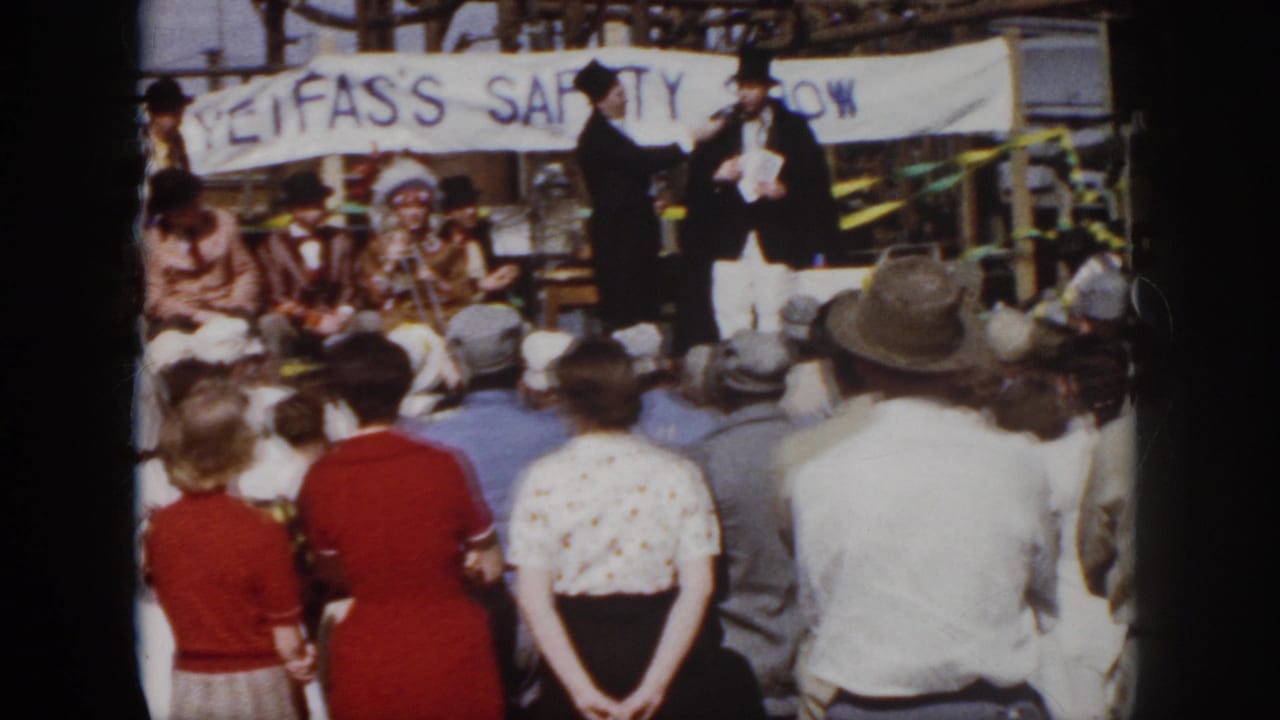 1958 Virginia home-movie frame of top-hatted stage performers, seated participants, and spectators beneath a safety-show banner.