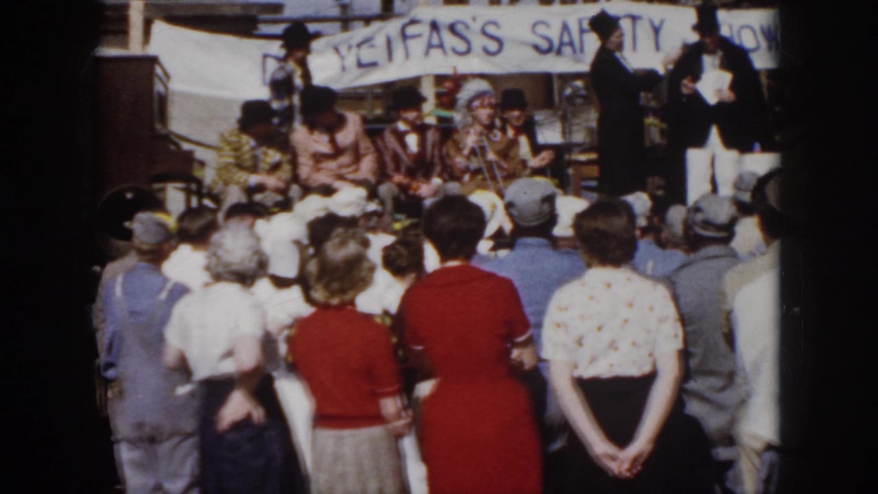 1958 Virginia frame showing an outdoor safety-show stage, spectators, costumed performers, and scaffolding in the background.