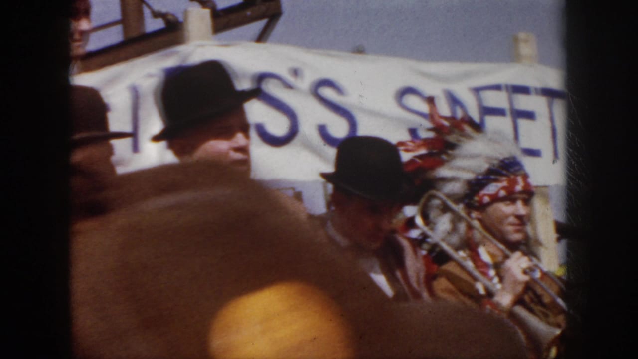 1958 Virginia parade frame with suited men on a float beside a performer in a feathered theatrical headdress holding a trombone.
