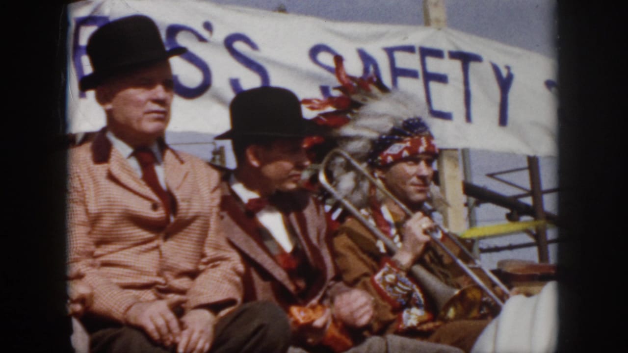 1958 Virginia home-movie frame showing suited men on a parade float and a trombone player seated below a safety banner.