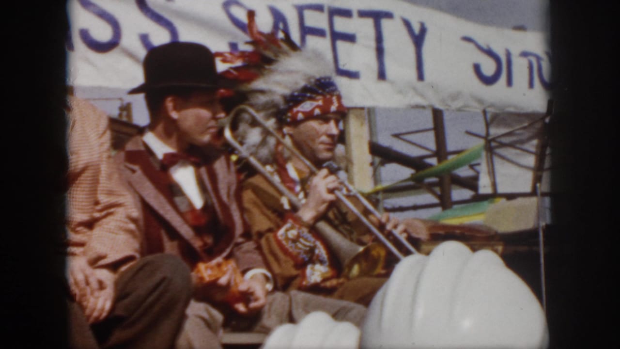 1958 Virginia 8mm frame showing a staged safety event with a trombone player, seated suited man, hard hats, and a partial SAFETY SHOW banner.