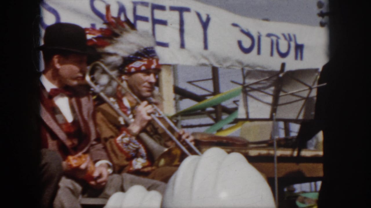 1958 Virginia workplace safety event frame with performers seated onstage, a readable SAFETY SHOW banner, and hard hats in the audience foreground.