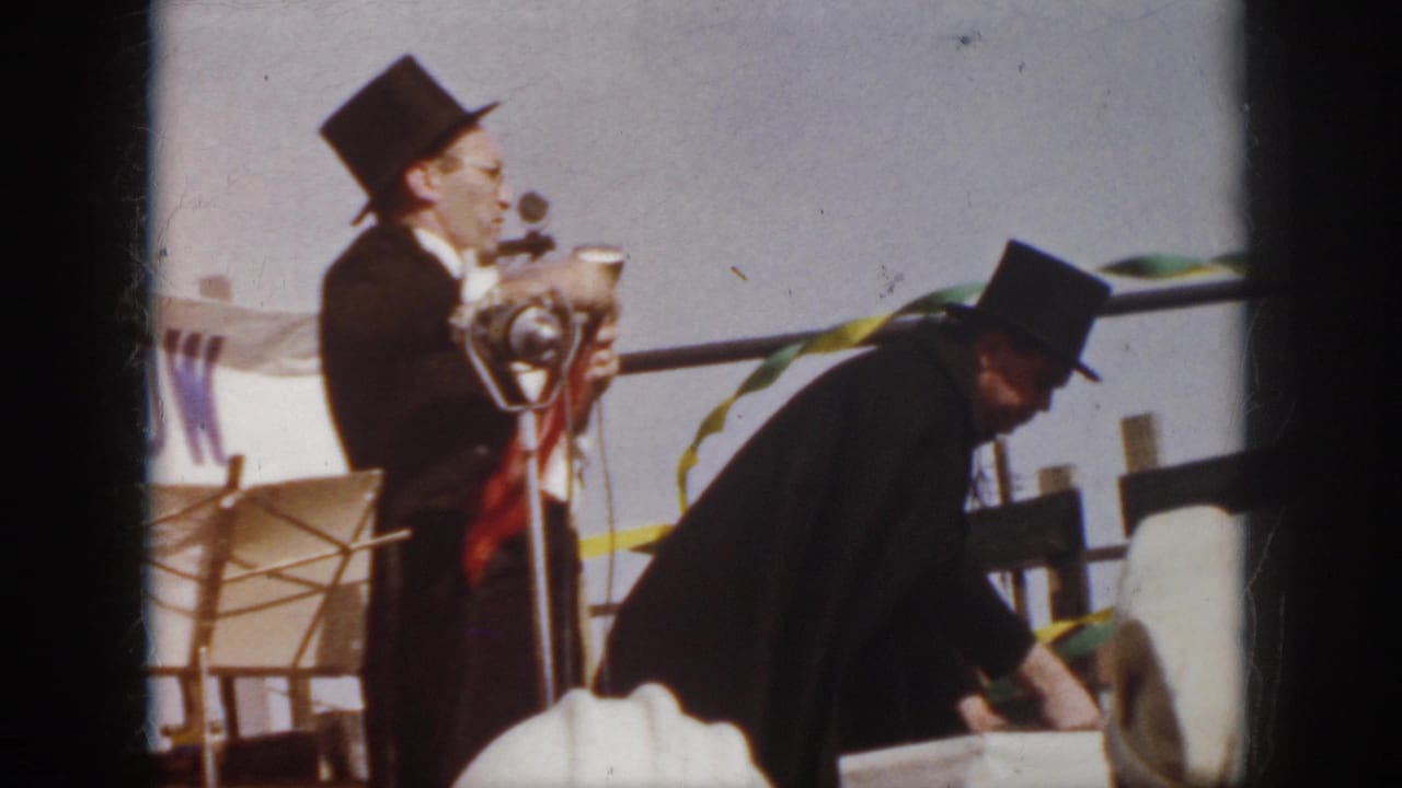 1958 Virginia 8mm still of a top-hatted magician holding a red handkerchief near a microphone during an outdoor stage act.